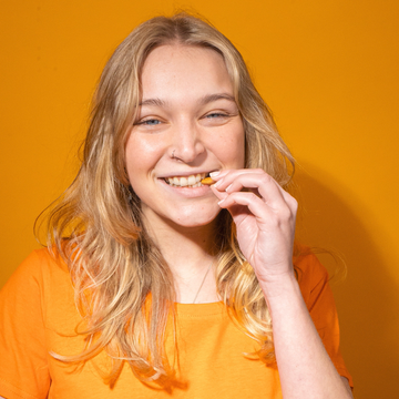 Eine lächelnde Frau isst Chips vor einem orangefarbenen Hintergrund.